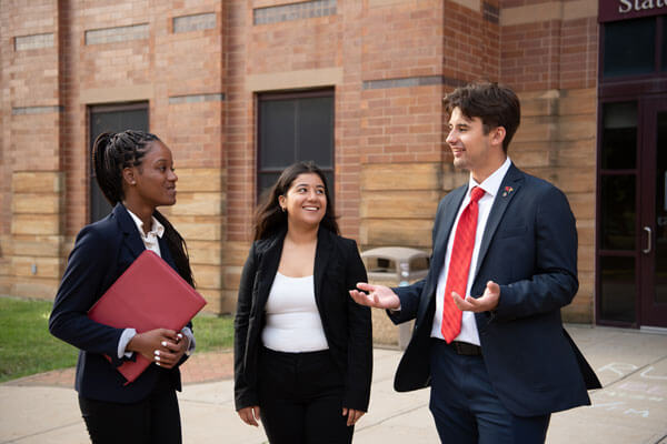 Three students in business attire chat on the quad.