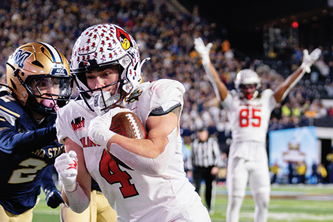 foreground is football player running with ball with backgrounding having football player cheering