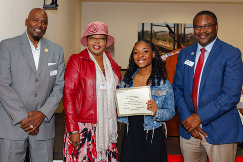 four people standing with one in middle holding scholarship award