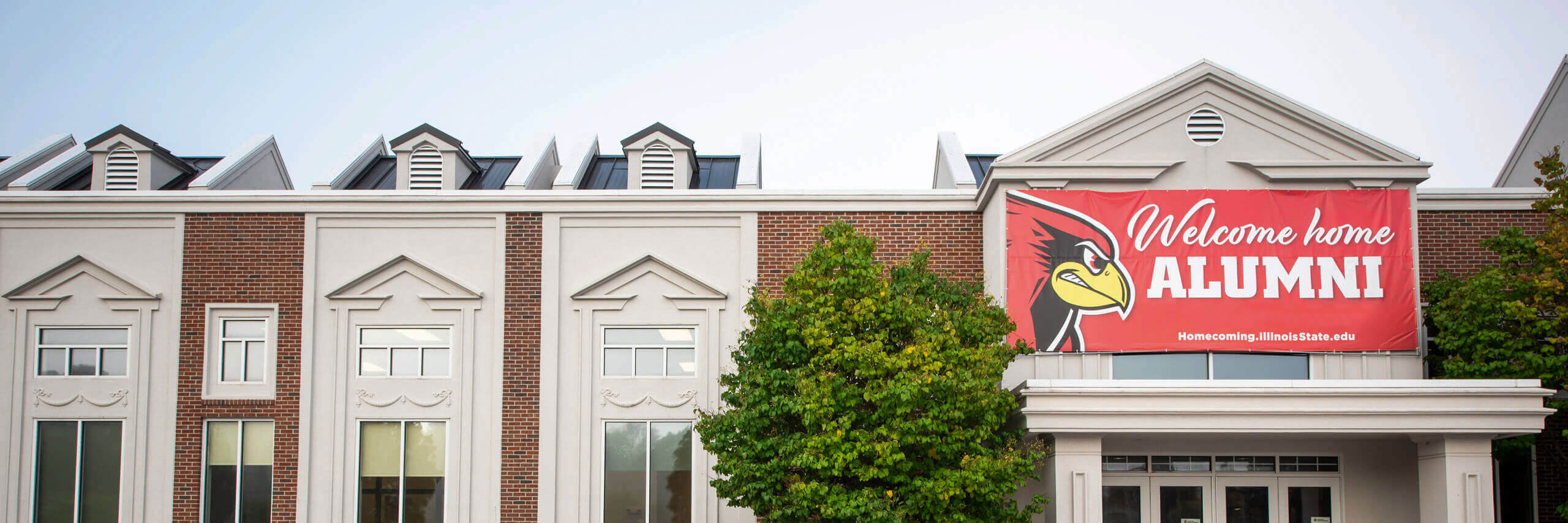 A banner reading 'Welcome Home, Alumni' hangs on the Alumni Center.